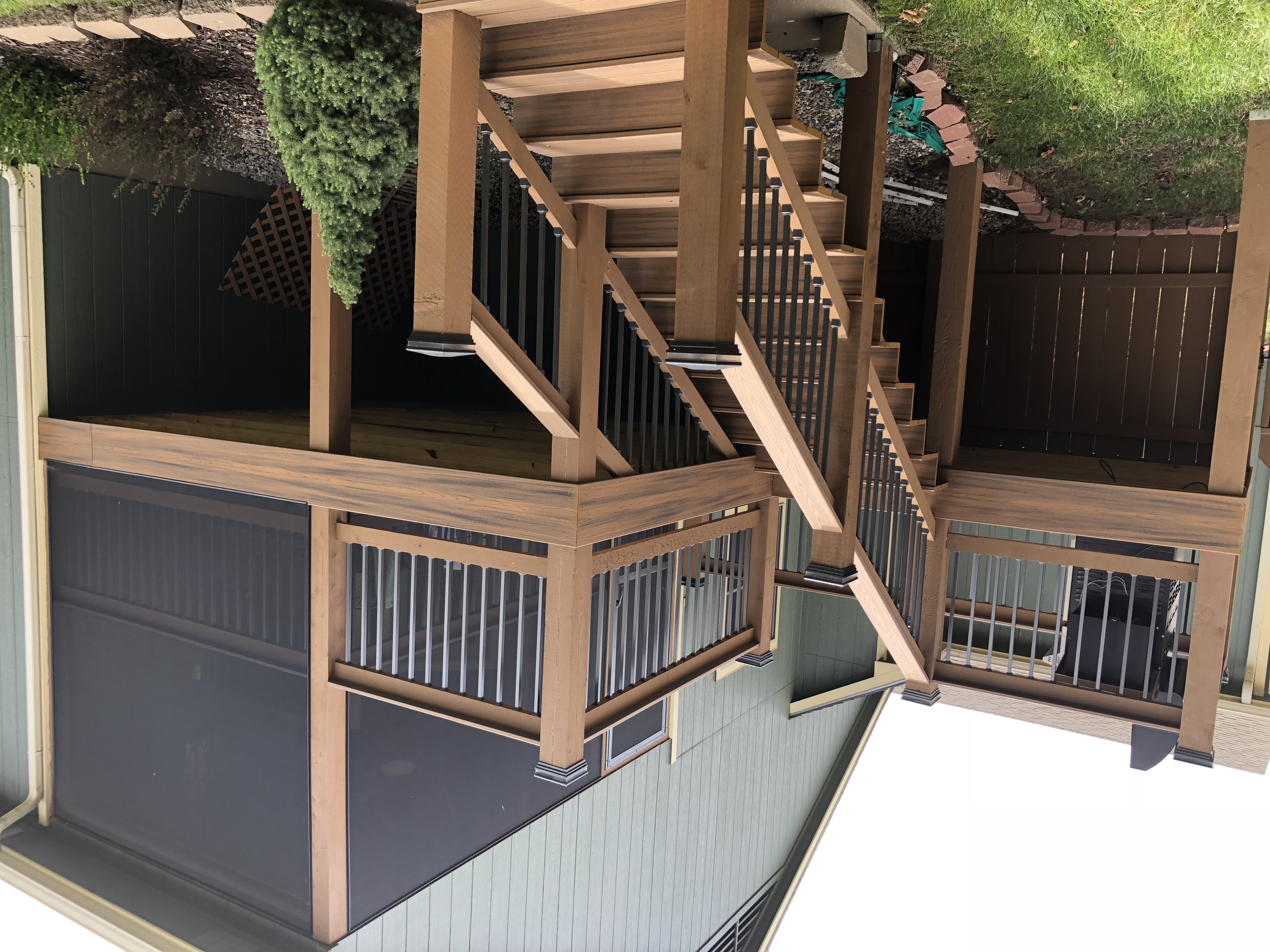 brown deck with a roof surrounded by a screen and an outdoor patio with stairs leading down