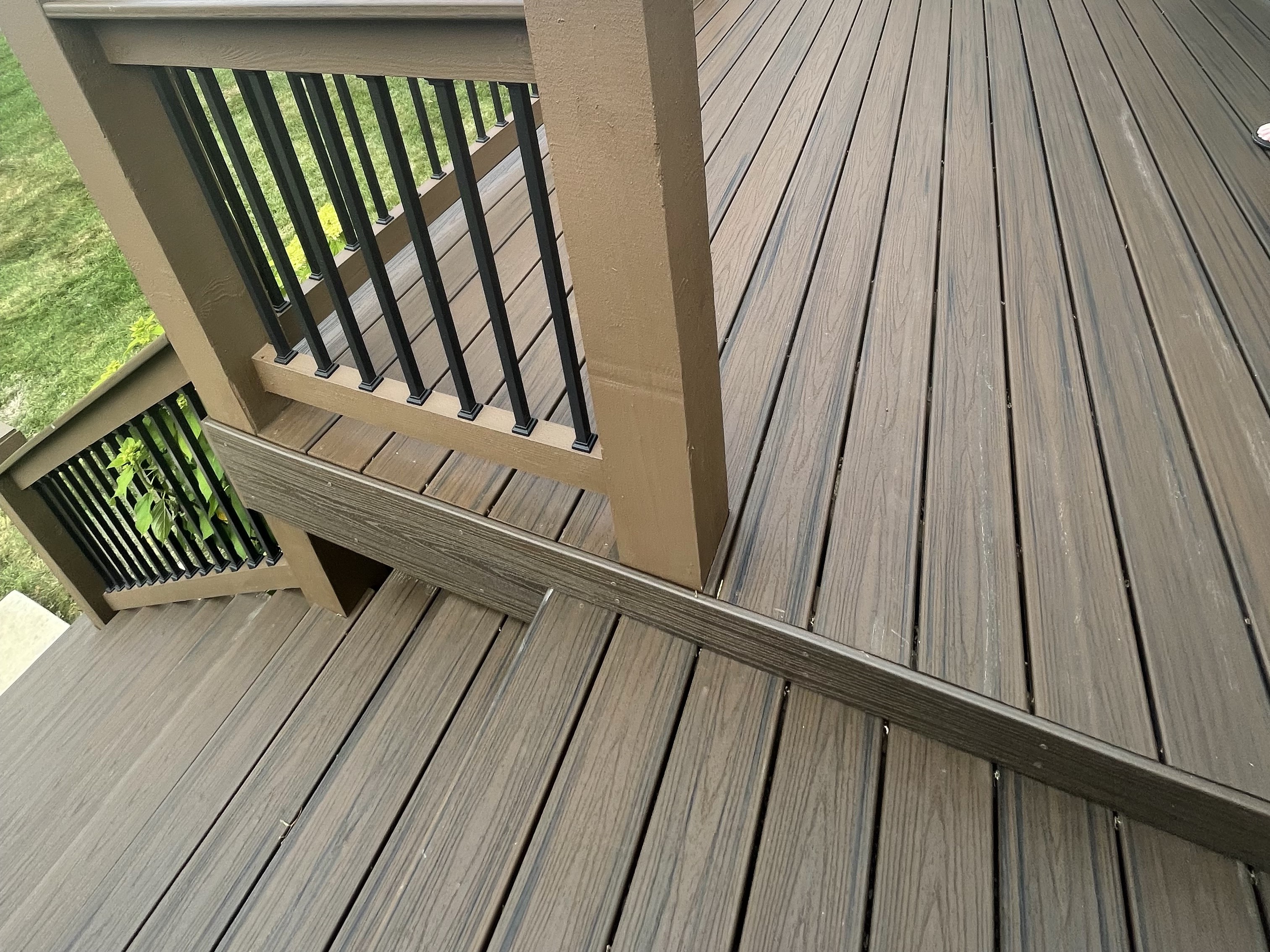 brown composite deck flooring with stairs that lead down with brown and black railing