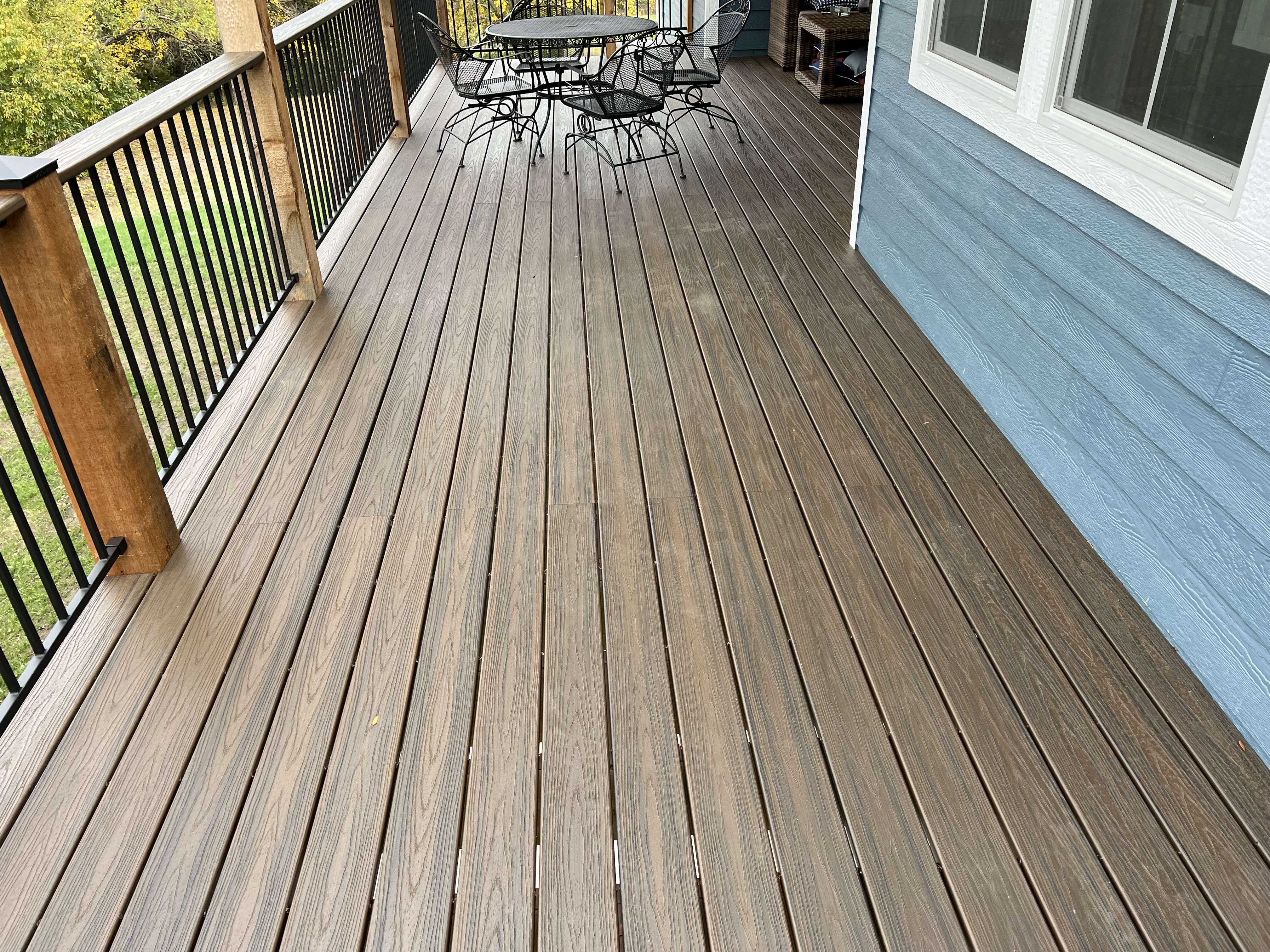 light brown deck flooring with black railing that has brown posts and table with chairs on the far side