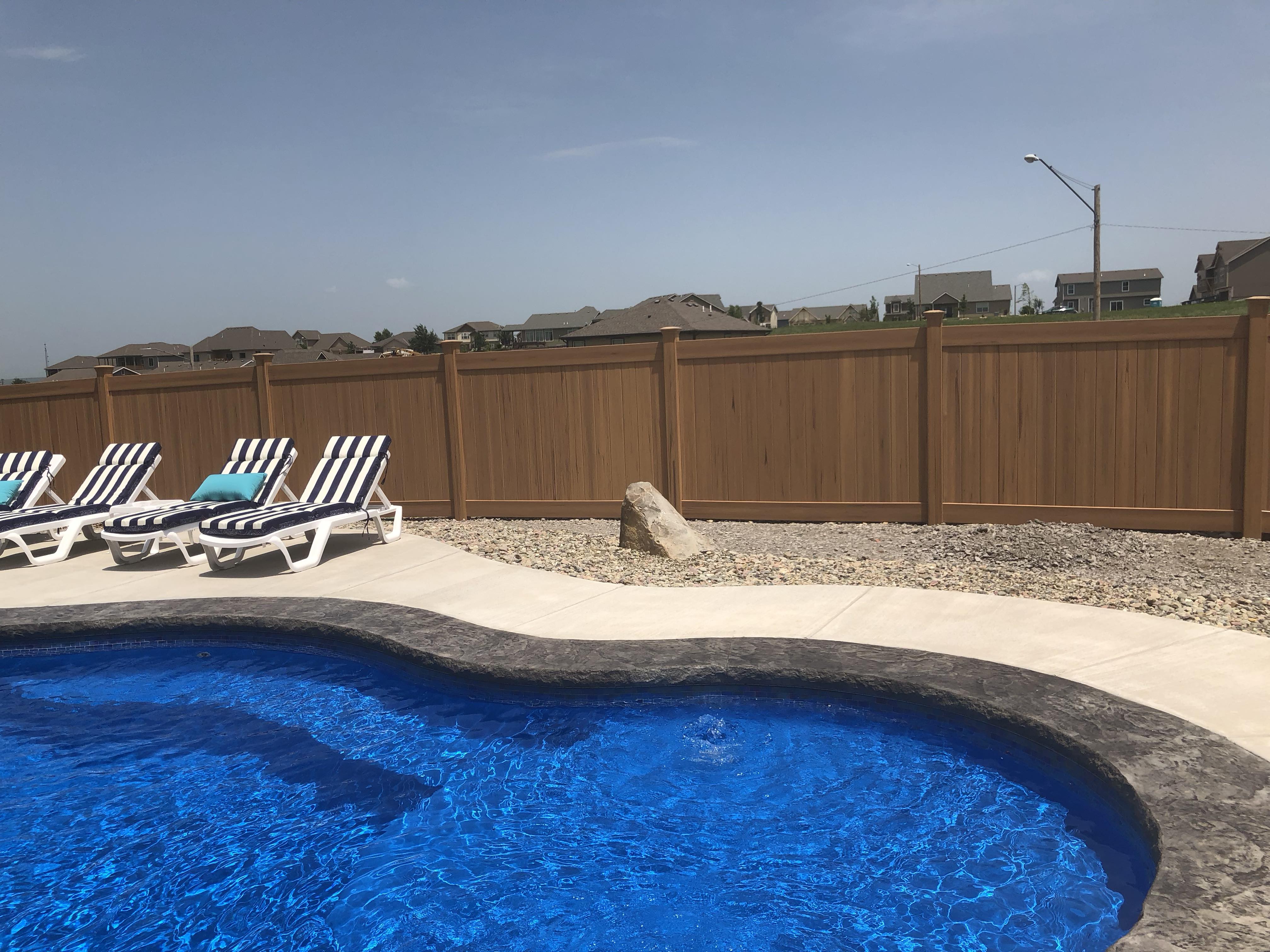 tall privacy brown vinyl fence with a pool in front of it