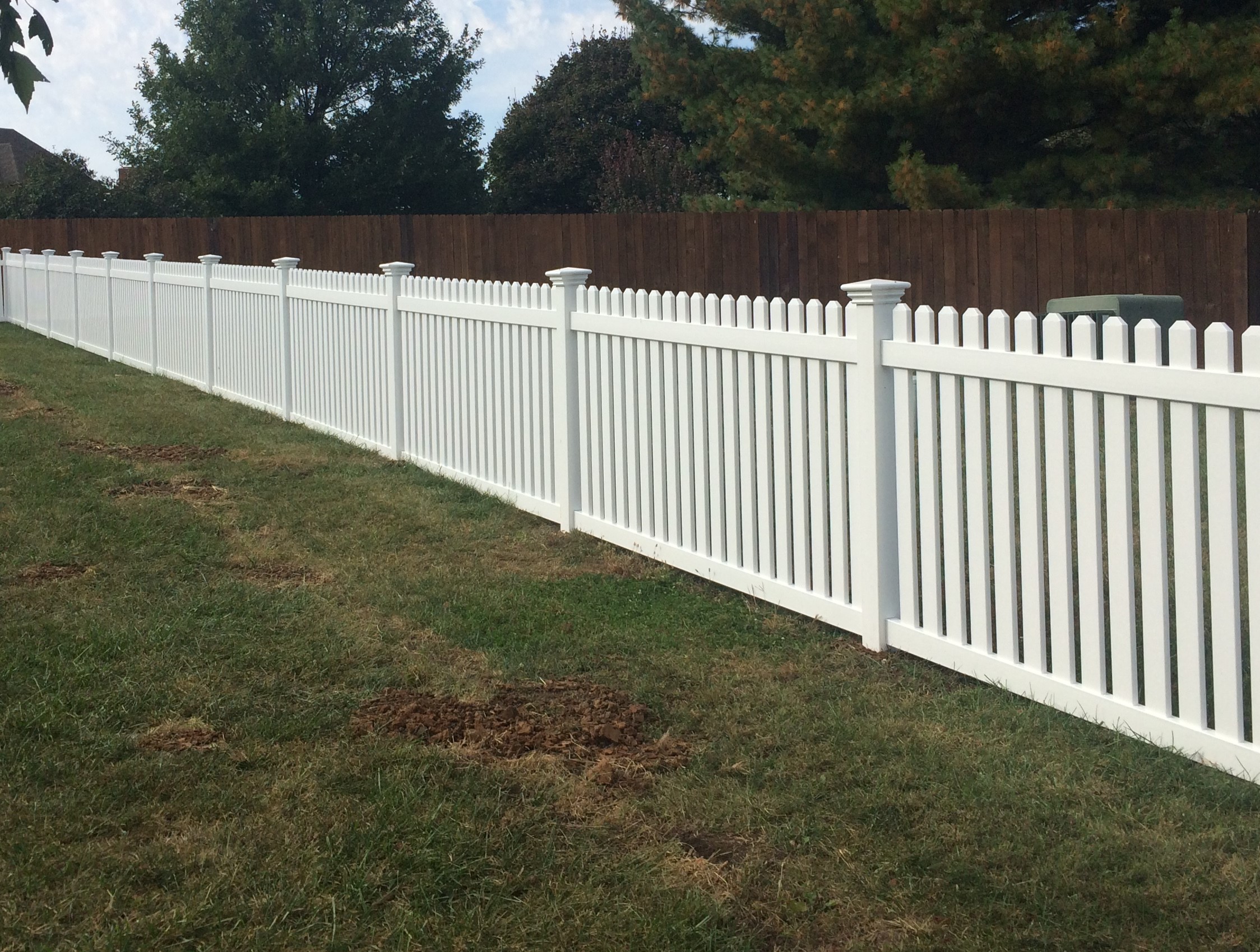 small white vinyl fence with an arch covering a corner and a tree