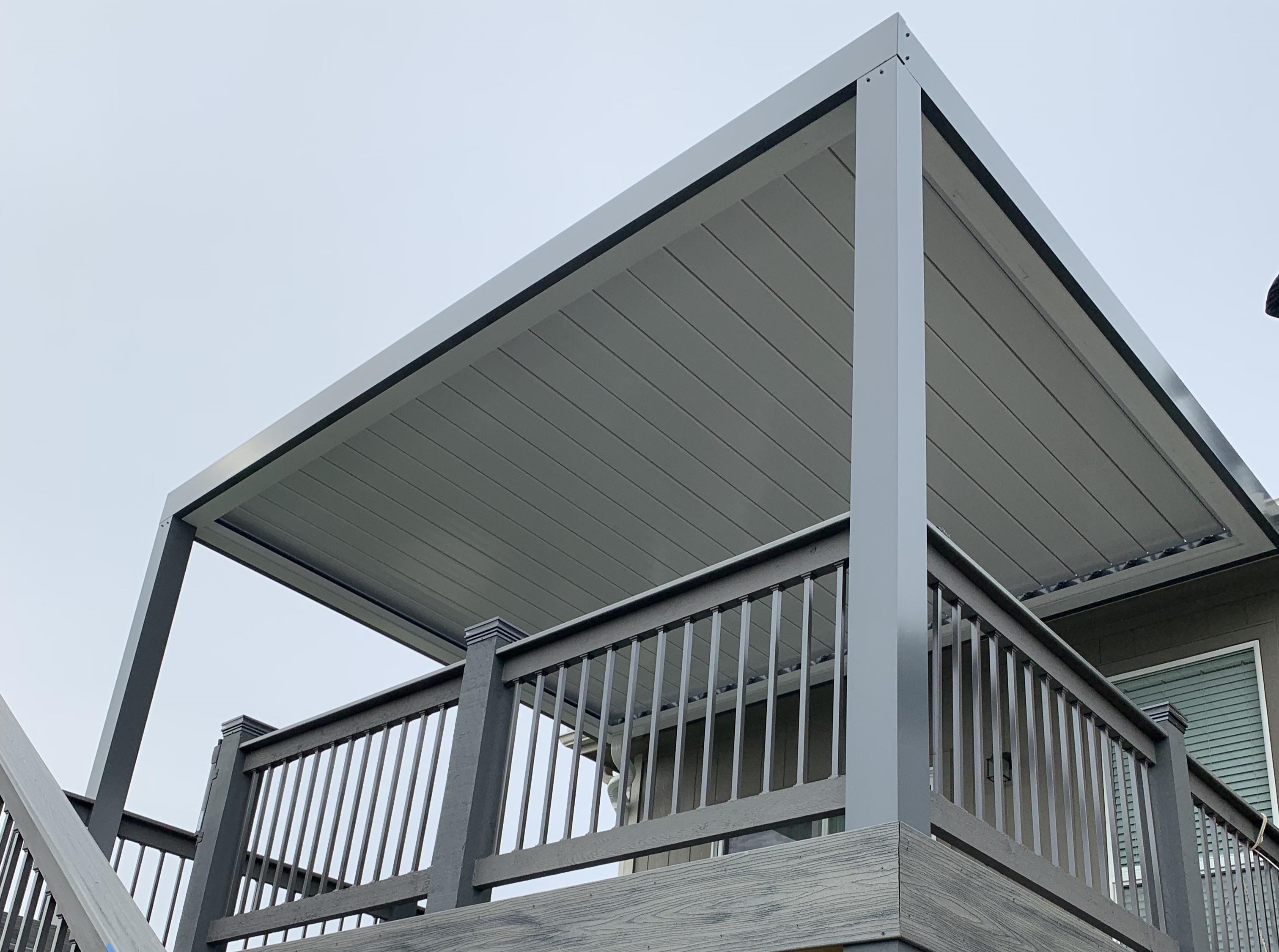 gray pergola over a gray deck with stairs outside a backyard