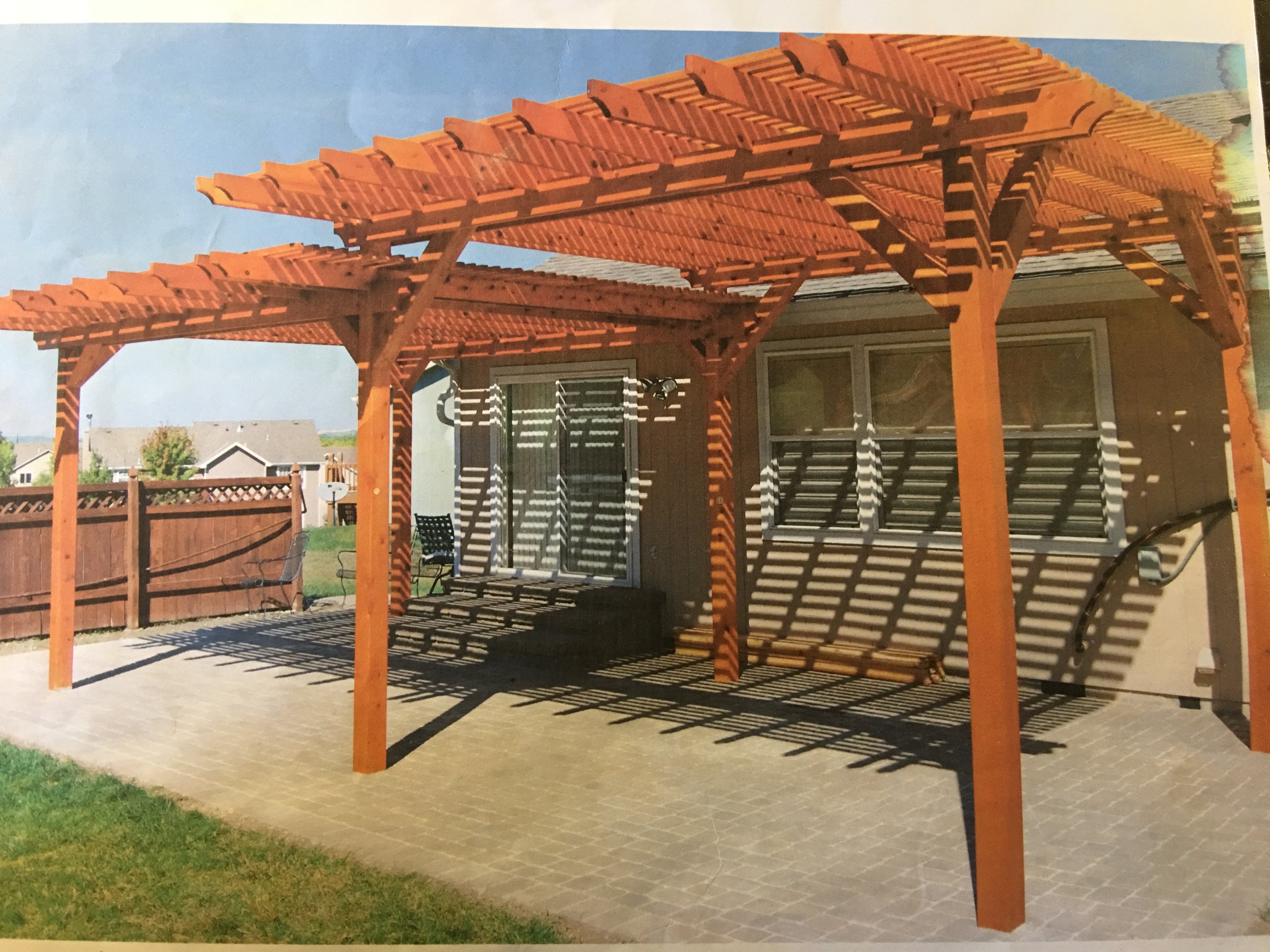 two red wood pergolas with intertwining tops over a concrete slab in a backyard